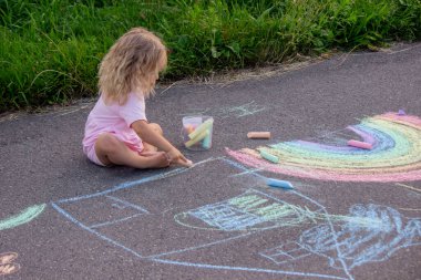 Küçük kız yazın asfalta renkli tebeşirle parlak bir gökkuşağı çiziyor.