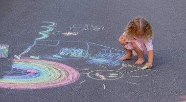 Küçük kız yazın asfalta renkli tebeşirle parlak bir gökkuşağı çiziyor.