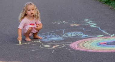 Küçük kız yazın asfalta renkli tebeşirle parlak bir gökkuşağı çiziyor.