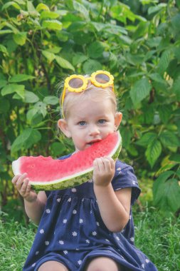 Büyük karpuz dilimli mutlu çocuk, yaz bahçesinde neşeli küçük kız.