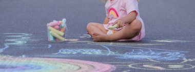 Sevimli küçük kız asfalt yolda tebeşirle renkli bir gökkuşağı çiziyor..