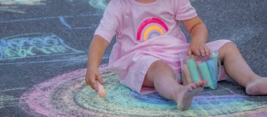 Sevimli küçük kız asfalt yolda tebeşirle renkli bir gökkuşağı çiziyor..