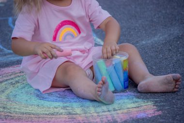 Sevimli küçük kız asfalt yolda tebeşirle renkli bir gökkuşağı çiziyor..