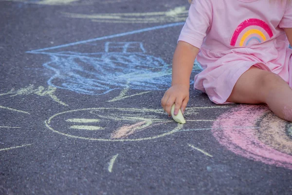 Sevimli küçük kız asfalt yolda tebeşirle renkli bir gökkuşağı çiziyor..