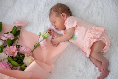 Yeni doğmuş bebek bir buket çiçeğin yanında sahte kürkün üzerinde uyuyor.