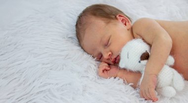 Yeni doğmuş bebek uyuyor ve beyaz bir oyuncak ayıya sarılıyor..