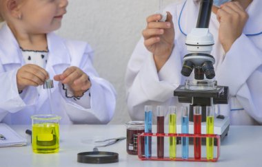 Laboratuvar önlükleriyle mikroskop ve test tüpleriyle oynayan sevimli çocuklar..