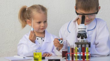 Laboratuvar önlükleriyle mikroskop ve test tüpleriyle oynayan sevimli çocuklar..