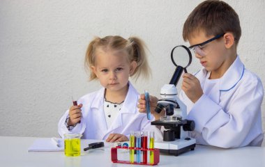 Laboratuvar önlükleriyle mikroskop ve test tüpleriyle oynayan sevimli çocuklar..