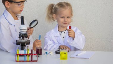 Laboratuvar önlükleriyle mikroskop ve test tüpleriyle oynayan sevimli çocuklar..