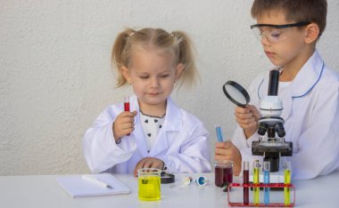 Laboratuvar önlükleriyle mikroskop ve test tüpleriyle oynayan sevimli çocuklar..