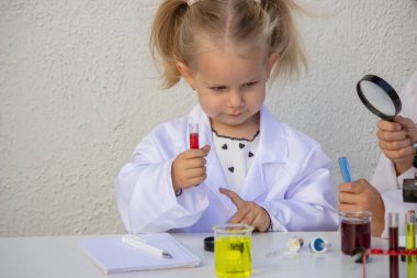 Bilim deneyi sırasında laboratuvar önlüklü küçük kız elinde kırmızı sıvıyla test tüpü tutuyordu..