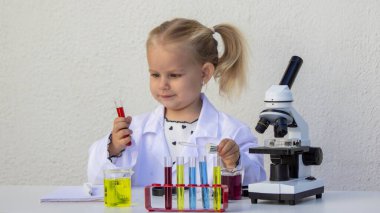 Bilim deneyi sırasında laboratuvar önlüklü küçük kız elinde kırmızı sıvıyla test tüpü tutuyordu..