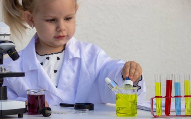 Laboratuvar önlüklü şirin küçük kız pipetle bilimsel deney yapıyor..