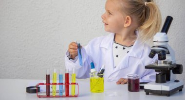 Laboratuvar önlüklü mutlu küçük kız elinde mavi bir tüp tutuyor..