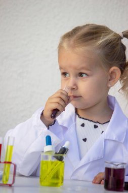 Laboratuvar önlüklü küçük kız bilim projesi için mor sıvıyla test tüpü tutuyor..