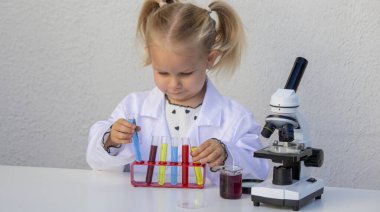 Laboratuvar önlüklü mutlu küçük kız elinde mavi bir tüp tutuyor..