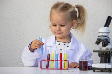 Laboratuvar önlüklü mutlu küçük kız elinde mavi bir tüp tutuyor..