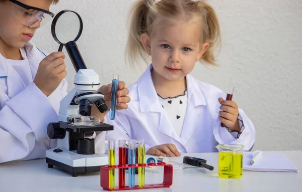 Laboratuvar önlükleriyle mikroskop ve test tüpleriyle oynayan sevimli çocuklar..