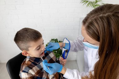 Pediatrik dişçi bir klinikte küçük çocuğun dişlerini muayene ediyor..