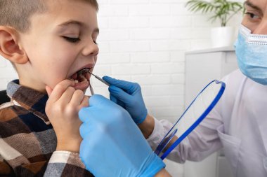 Pediatrik dişçi bir klinikte küçük çocuğun dişlerini muayene ediyor..