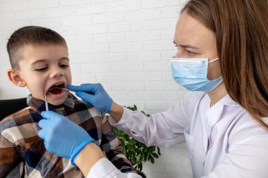 Pediatrik dişçi bir klinikte küçük çocuğun dişlerini muayene ediyor..