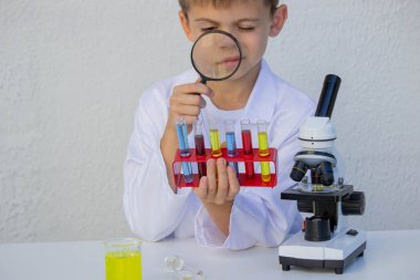 Küçük çocuk renkli test tüplerini büyüteçle inceliyor..