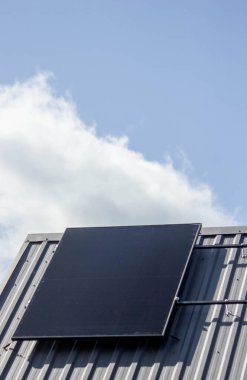 Güneş paneli mavi gökyüzünün altındaki özel bir evin metal çatısına kurulmuş..