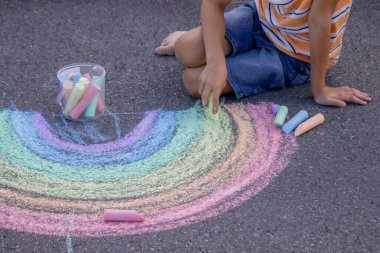 Çocukların elleri gri asfalta renkli bir tebeşir gökkuşağı çiziyor - yaratıcı yaz aktivitesi.