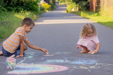 Güneşli bir yaz gününde parkta tebeşirle çizim yapan iki kardeş..