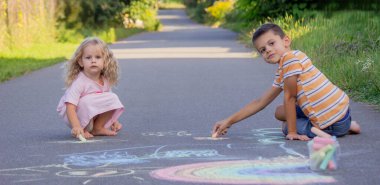 Güneşli bir yaz gününde parkta tebeşirle çizim yapan iki kardeş..