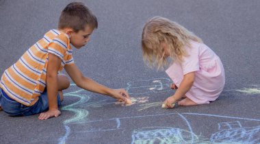 Güneşli bir yaz gününde parkta tebeşirle çizim yapan iki kardeş..
