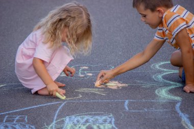 Güneşli bir yaz gününde parkta tebeşirle çizim yapan iki kardeş..