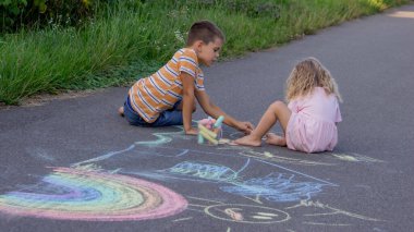 Güneşli bir yaz gününde parkta tebeşirle çizim yapan iki kardeş..