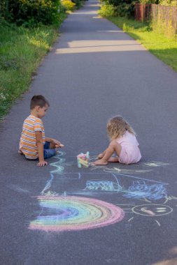 Güneşli bir yaz gününde parkta tebeşirle çizim yapan iki kardeş..