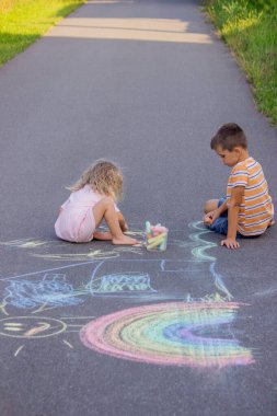 Güneşli bir yaz gününde parkta tebeşirle çizim yapan iki kardeş..