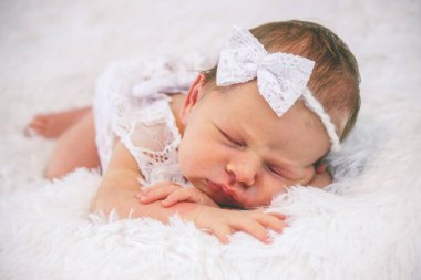 Beyaz dantelli elbise ve saç bandıyla tüylü bir battaniyede uyuyan yeni doğmuş bebek.