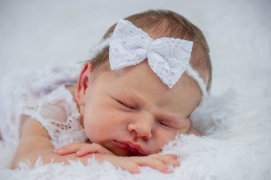 Beyaz dantelli elbise ve saç bandıyla tüylü bir battaniyede uyuyan yeni doğmuş bebek.