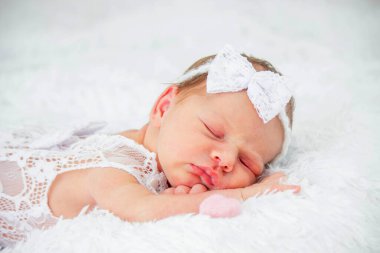 Beyaz dantelli elbise ve saç bandıyla tüylü bir battaniyede uyuyan yeni doğmuş bebek.