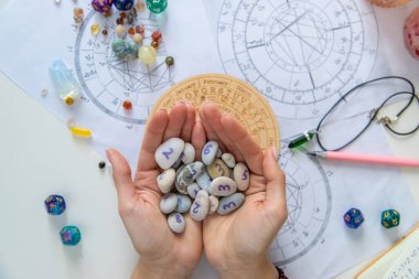 Astrolog, doğum çizelgeleri ve zodyak çarkının üzerinde sayıbilim taşlarını tutuyor..