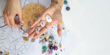 Astrolog, doğum çizelgeleri ve zodyak çarkının üzerinde sayıbilim taşlarını tutuyor..