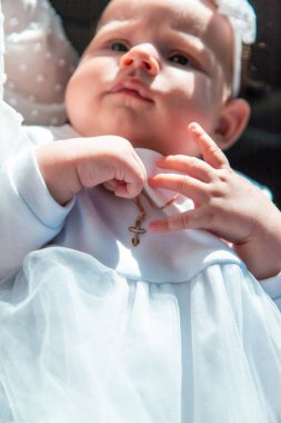 Bebeğin Vaftizleri: Küçük bir haç kolyesi ve beyaz saç bandıyla küçük bir kız çocuğu