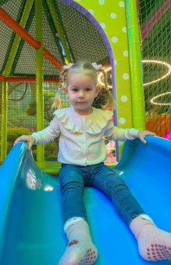 At kuyruklu küçük kız bir çocuk oyun merkezinde mavi bir kaydıraktan kayıyor..