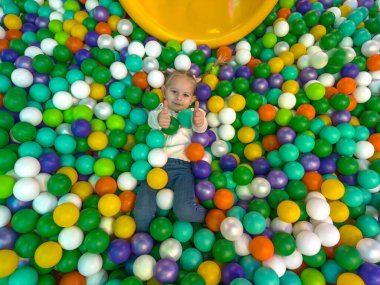Mutlu çocuk, parlak renkli plastik toplarla kuru bir top havuzunda yatıyor..