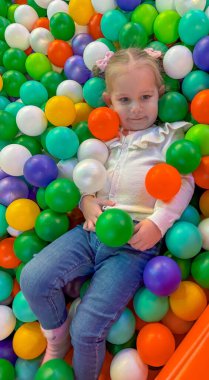 Mutlu çocuk, parlak renkli plastik toplarla kuru bir top havuzunda yatıyor..