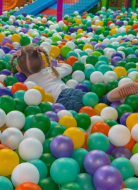 Mutlu çocuk, parlak renkli plastik toplarla kuru bir top havuzunda yatıyor..
