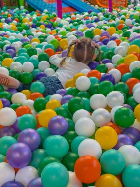 Mutlu çocuk, parlak renkli plastik toplarla kuru bir top havuzunda yatıyor..