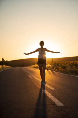 Genç bir kız, yalnız ve düz bir yolun ortasında yürüyor, günün geç saatlerinde. Elleri haç şeklinde gerilmiş, dengeyi sağlamak ve bölünme çizgisinden düşmemek için..