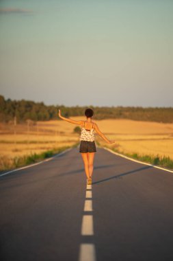 Genç bir kız, yalnız ve düz bir yolun ortasında yürüyor, günün geç saatlerinde. Elleri haç şeklinde gerilmiş, dengeyi sağlamak ve bölünme çizgisinden düşmemek için..