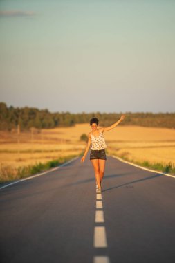 Genç bir kız, yalnız ve düz bir yolun ortasında yürüyor, günün geç saatlerinde. Elleri haç şeklinde gerilmiş, dengeyi sağlamak ve bölünme çizgisinden düşmemek için..